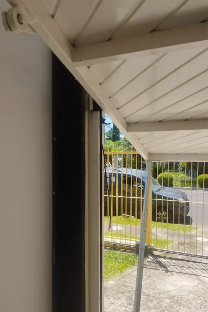 Vista interna de uma garagem exibindo a estrutura metálica superior de um portão eletrônico basculante parcialmente aberto para a rua.