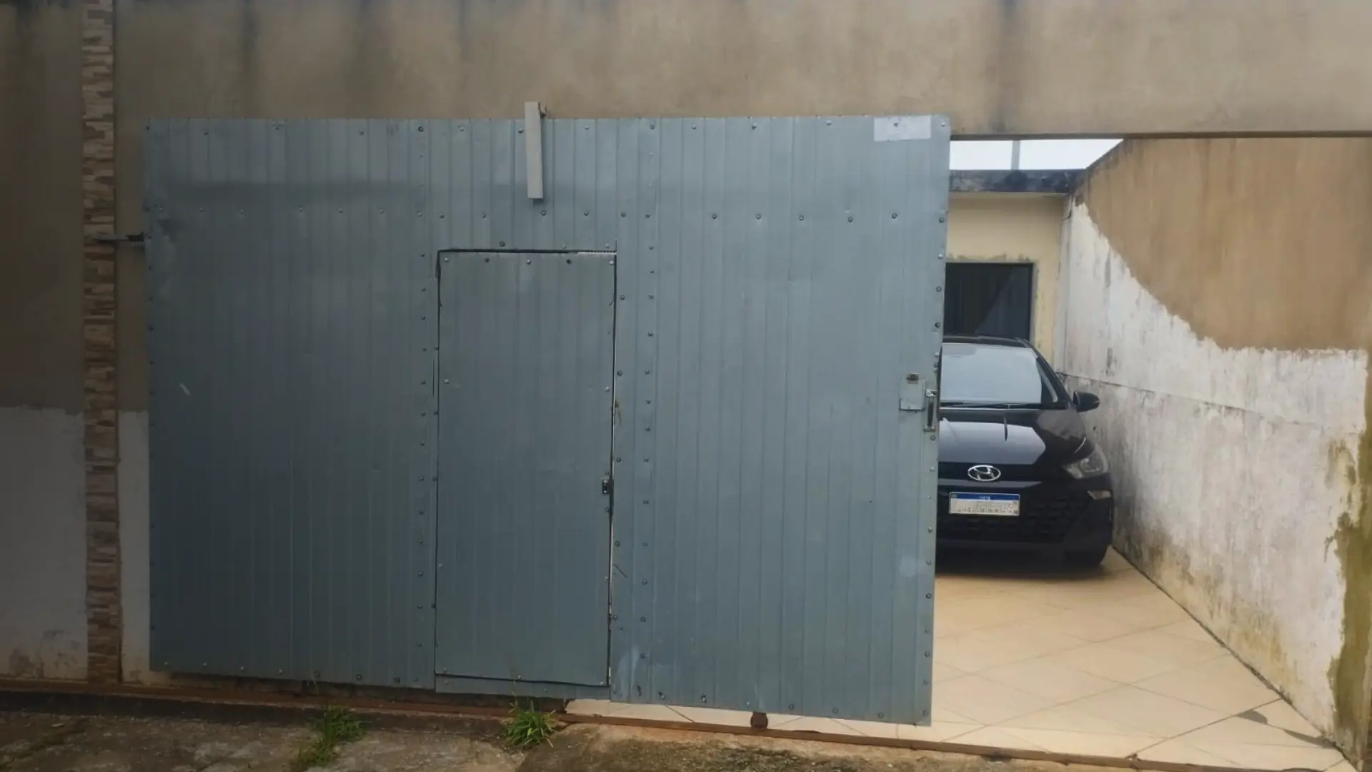 Portão eletrônico deslizante de chapa abrindo automaticamente em uma garagem residencial, após serviço completo de instalação.