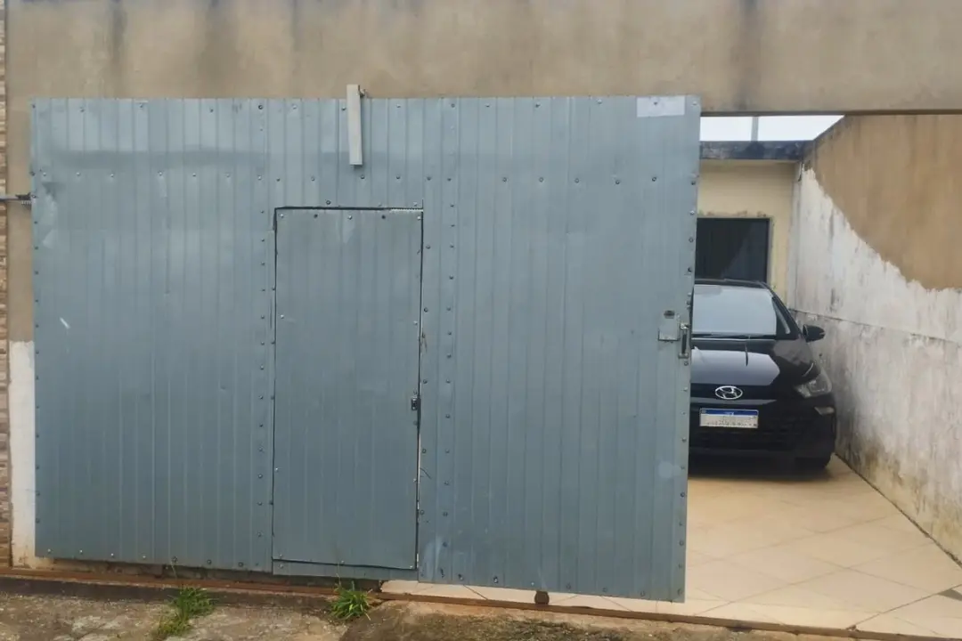 Portão eletrônico de chapa lisa cinza parcialmente aberto em garagem com carro preto estacionado de forma segura no interior.